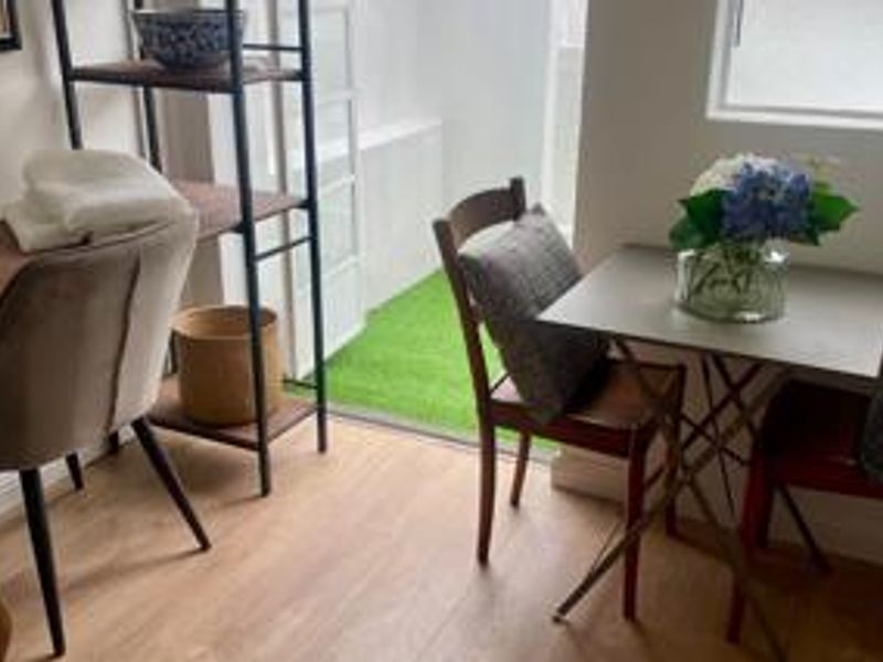 A bright living area featuring light wood-look laminate flooring and a sliding glass door providing direct access to a small artificial grass patio.