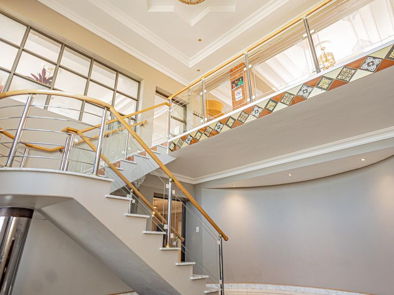 Grand entrance foyer featuring a sweeping staircase with glass balustrades, decorative tile accents, and high ceilings with recessed lighting.