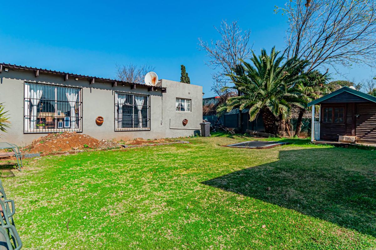 Rear view of the property featuring a spacious lawn, a garden shed, and security bars on the windows.