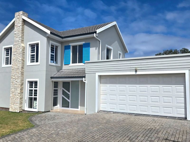 A well-maintained double-story home featuring a stone-clad chimney, paved driveway, double garage, and blue shutter accents on the windows.
