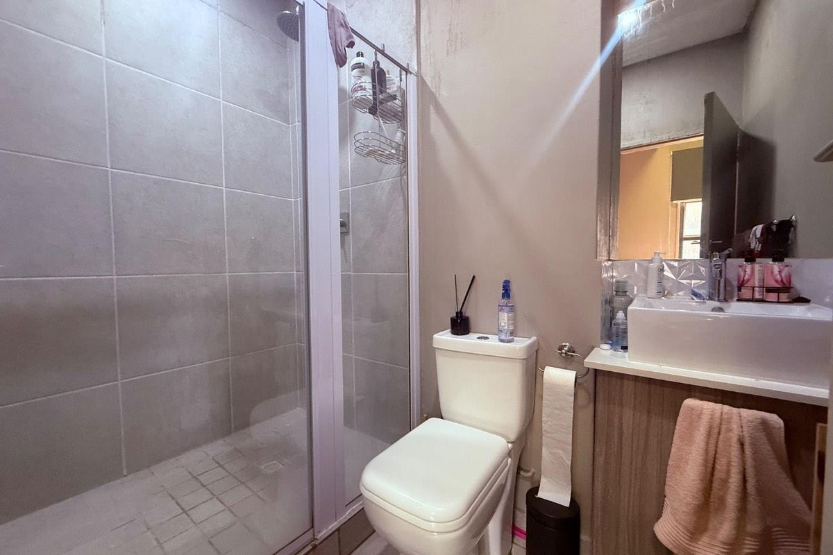 A functional bathroom featuring a glass-enclosed shower, a vanity with a basin, and a standard toilet, showing signs of wear on the walls.