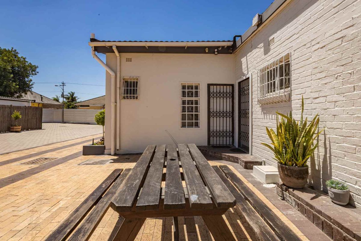 A paved rear courtyard area featuring white painted brick walls, security gates, and window bars, providing a functional outdoor space.