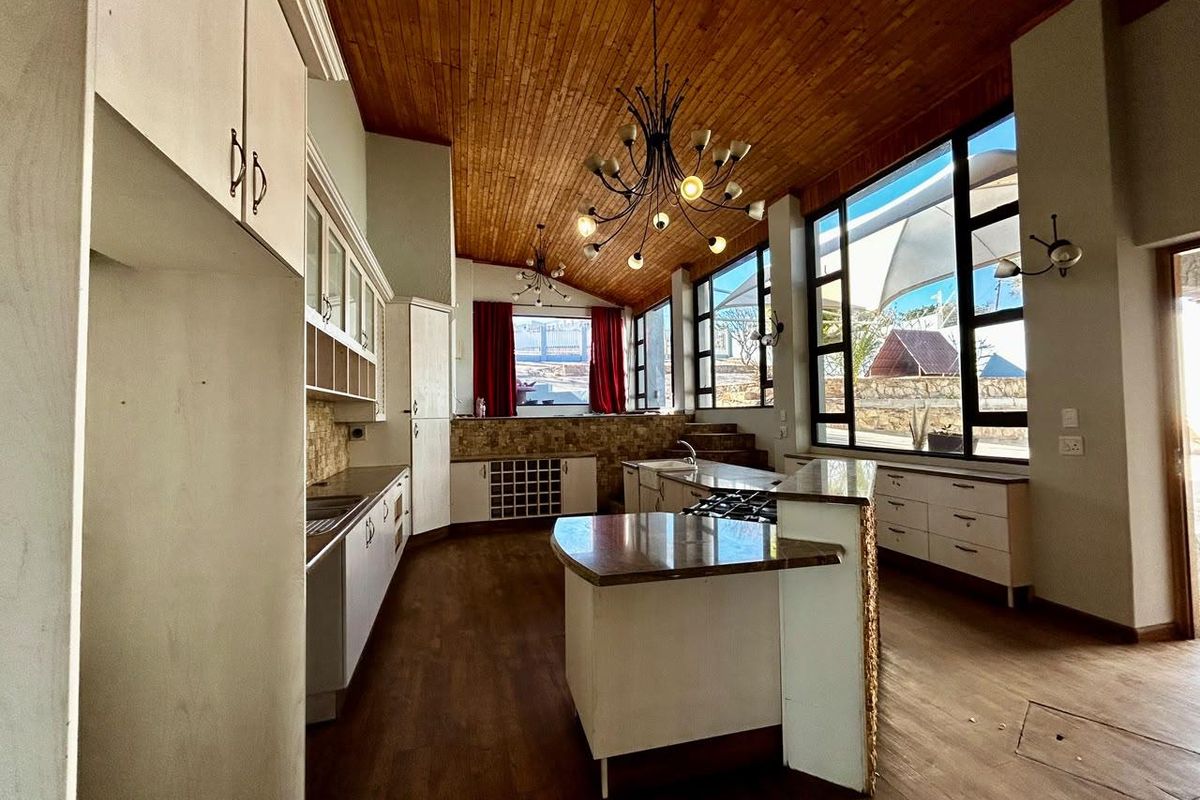 Spacious kitchen featuring a large island, stone countertops, timber ceiling, and expansive windows providing ample natural light.