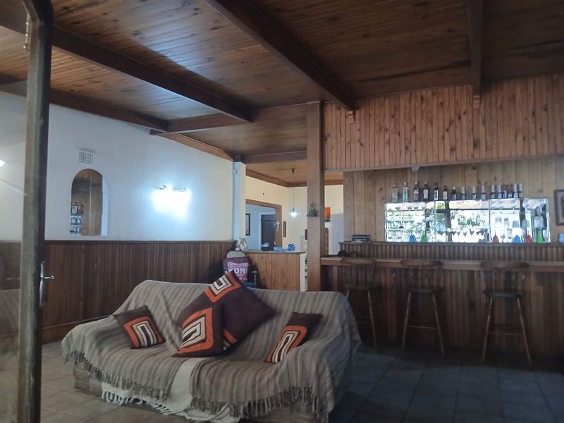 A rustic entertainment area featuring a built-in bar with timber paneling, mirrored shelving, exposed ceiling beams, and tiled flooring.