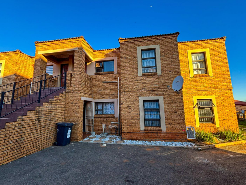 Front elevation of a double-storey face brick townhouse featuring an external staircase, security gates, and aluminium window frames with security bars.