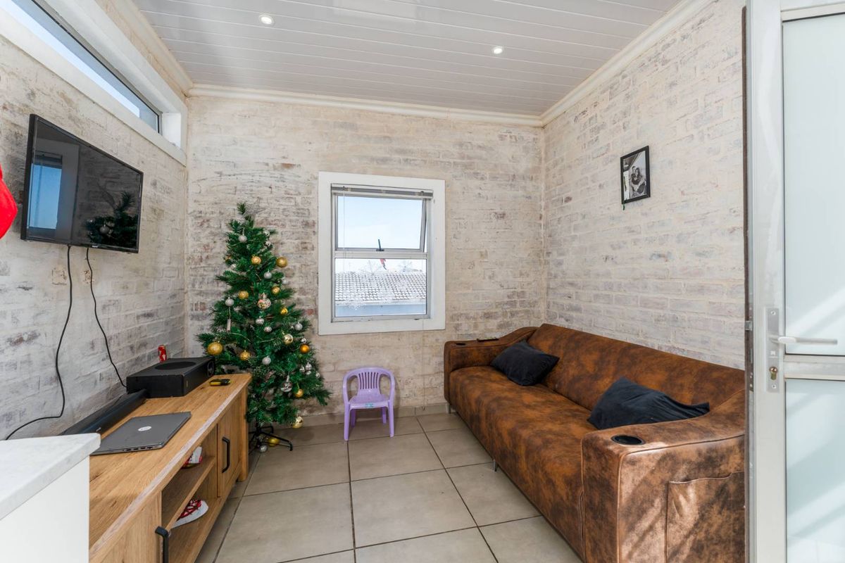 A compact living room featuring exposed whitewashed brick walls, tiled flooring, and a tongue-and-groove ceiling with recessed lighting.