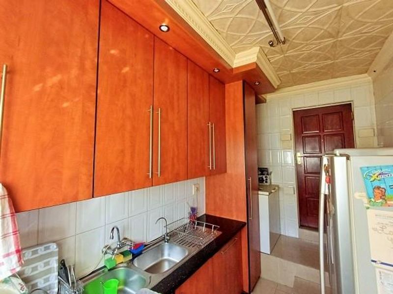 A functional kitchen featuring warm-toned laminate cabinetry, a double stainless steel sink, tiled splashbacks, and a distinctive textured ceiling with recessed lighting.
