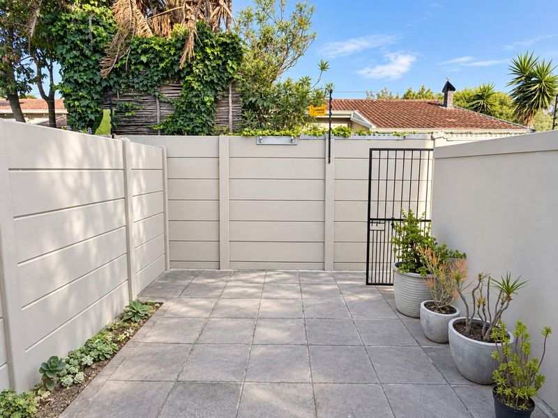 A private, paved rear courtyard area enclosed by high precast concrete walls and a secure metal gate, featuring low-maintenance succulent garden beds.