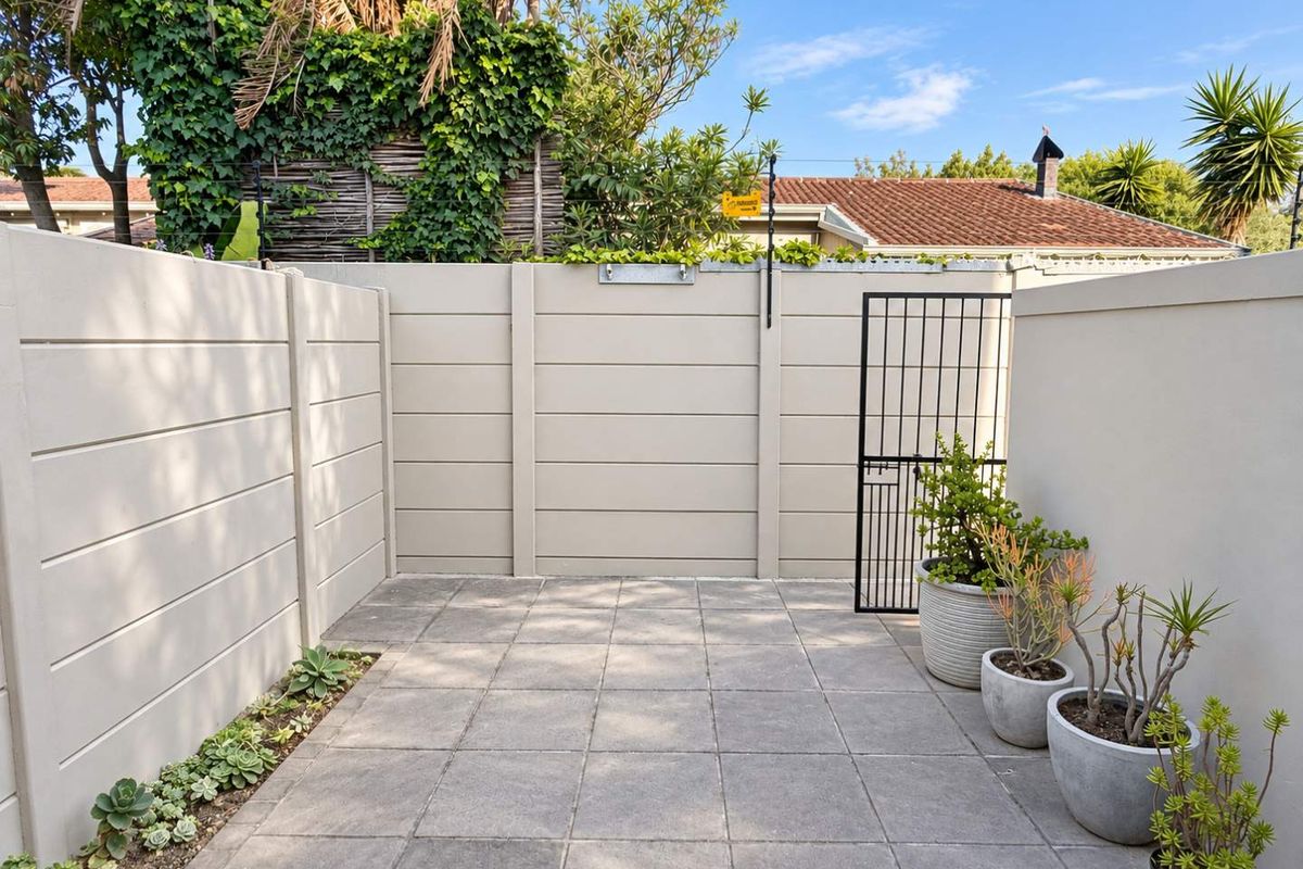 A private, paved rear courtyard area enclosed by high precast concrete walls and a secure metal gate, featuring low-maintenance succulent garden beds.