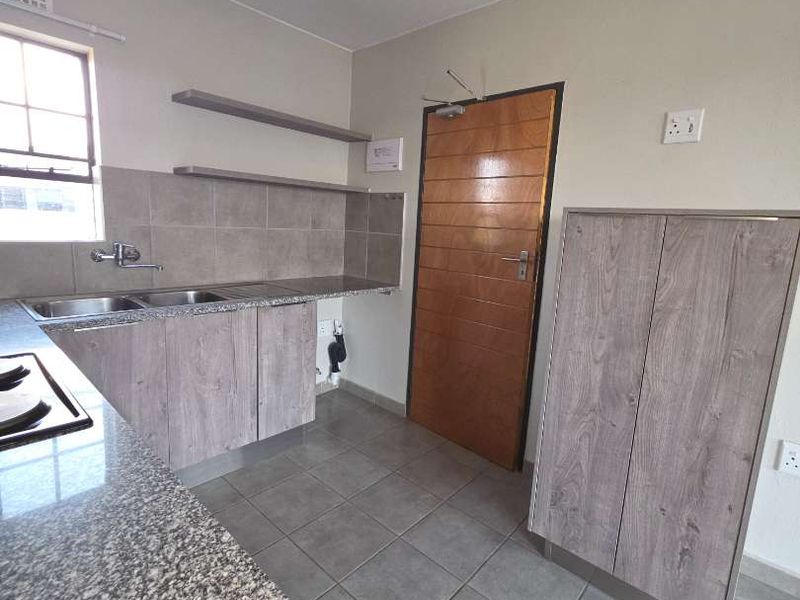 A clean, functional kitchen featuring granite countertops, built-in cabinetry, a double basin sink, and tiled flooring.