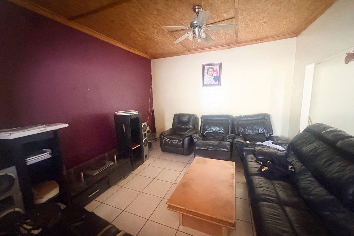 A living room featuring tiled flooring, a wooden ceiling with a mounted fan, and a prominent accent wall.