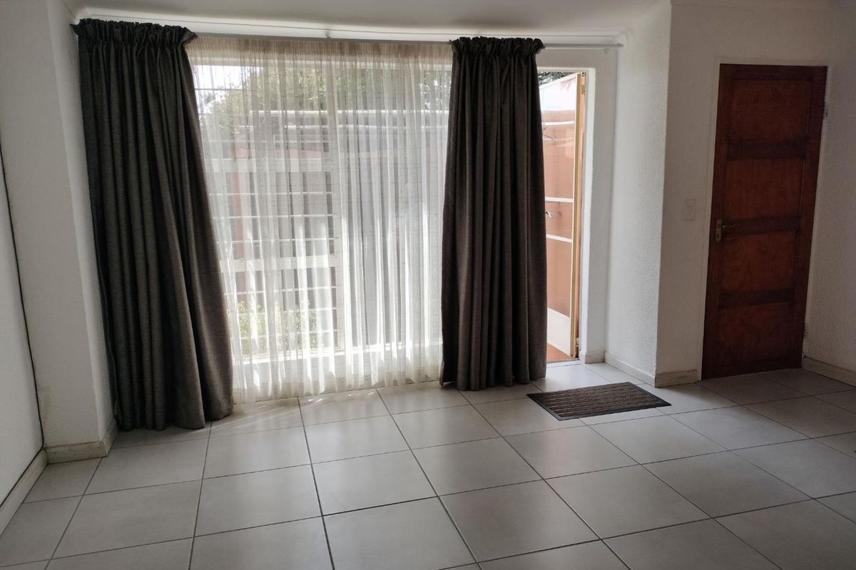 A bright living area featuring neutral floor tiles, large glass sliding doors with curtains, and direct access to an outdoor space.