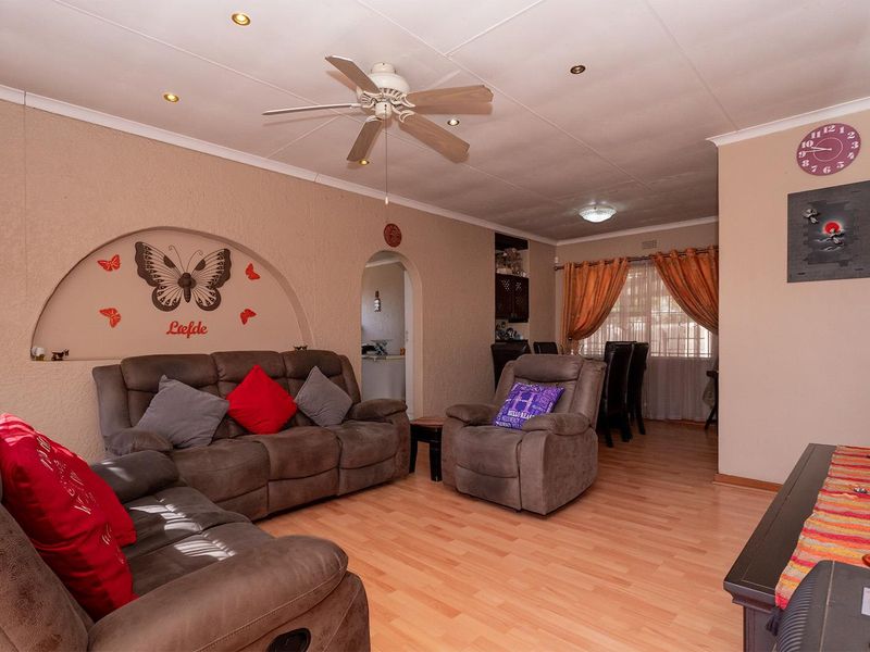 A spacious living room featuring laminate flooring, a ceiling fan, recessed lighting, and a decorative built-in wall niche, leading into an adjacent dining area.