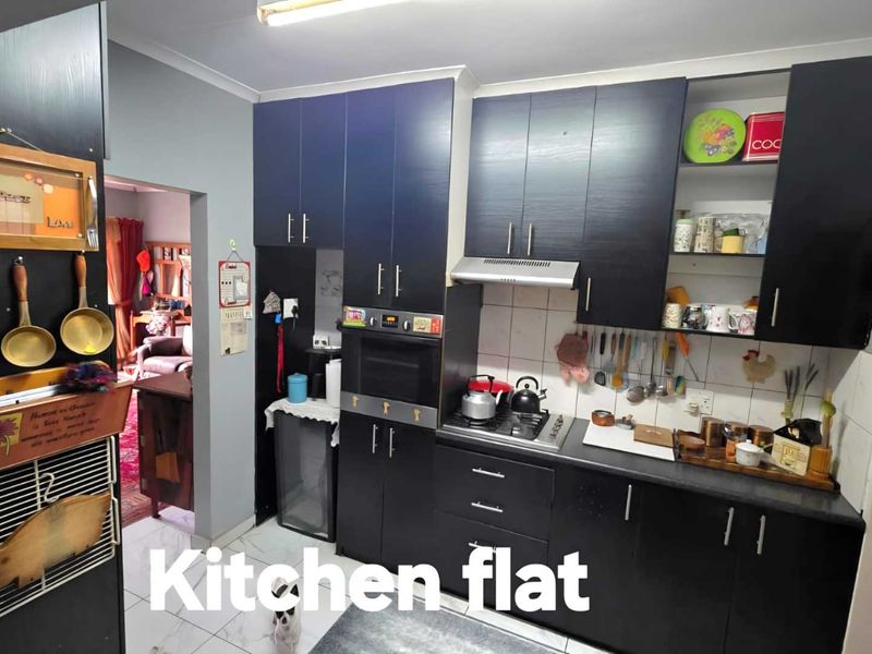 A functional kitchen featuring dark cabinetry, built-in oven, gas hob, and extractor fan, with tiled flooring and splashback.