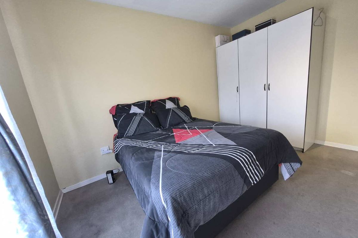 A bedroom featuring neutral wall paint, carpeted flooring, and a white built-in wardrobe providing ample storage space.