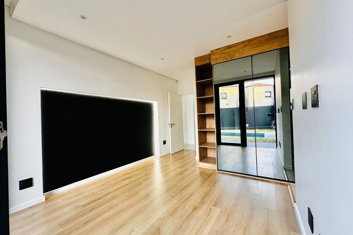 Modern bedroom featuring light laminate flooring, built-in mirrored cupboards with integrated shelving, and a sliding glass door providing access to the outdoor area.