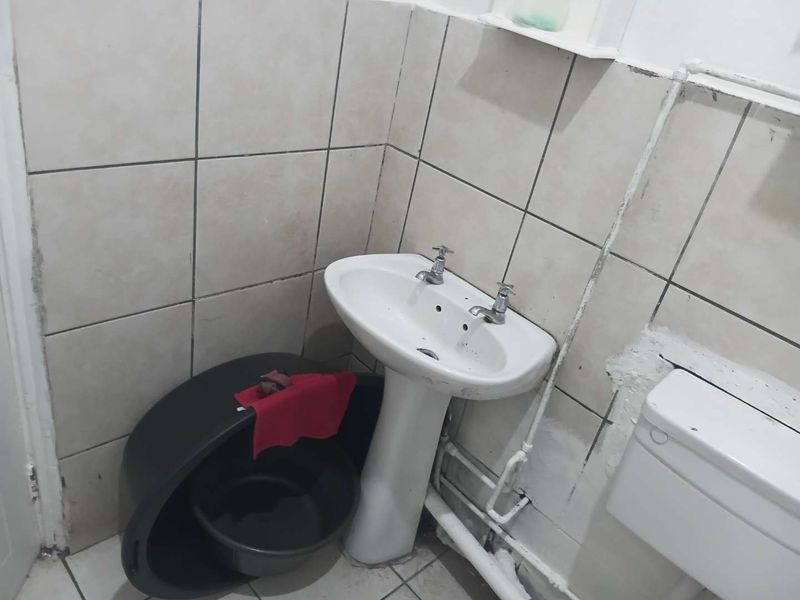 A small bathroom featuring a pedestal basin and tiled walls. The space requires cosmetic updates and improved finishing to the plumbing and wall surfaces.
