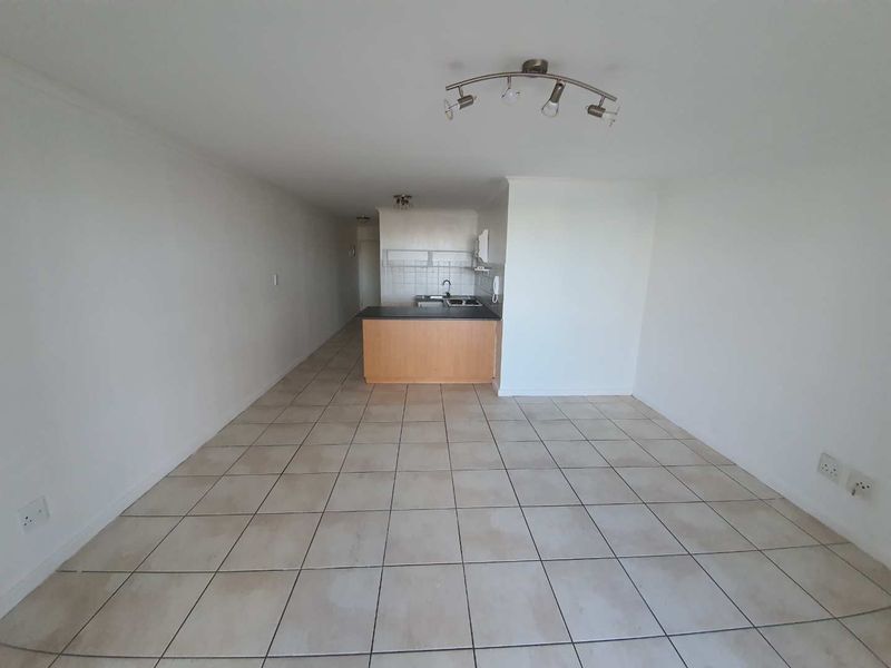 An empty open-plan living and kitchen area featuring tiled flooring, a compact kitchen counter with a sink, and a cooktop.