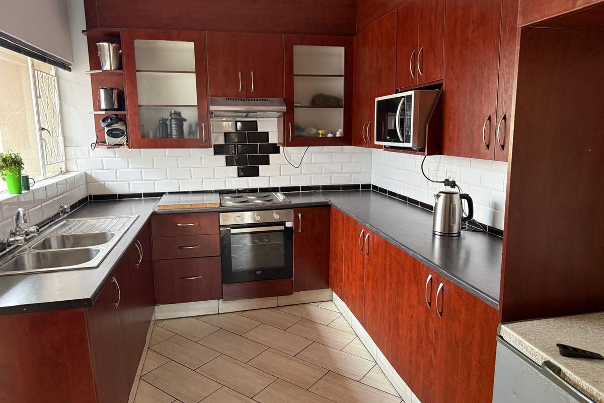 A functional kitchen featuring dark wood cabinetry, subway tile backsplash, laminate countertops, and integrated appliances including an oven and extractor fan.