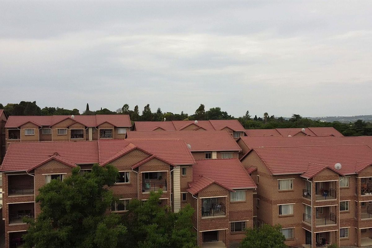 Aerial view of a multi-story apartment complex featuring facebrick facades and tiled roofing, showcasing the residential building layout and surrounding greenery.