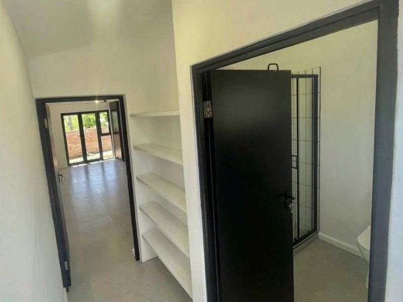 A clean, neutral hallway featuring built-in shelving, tiled flooring, and access to an adjacent bathroom and living area.