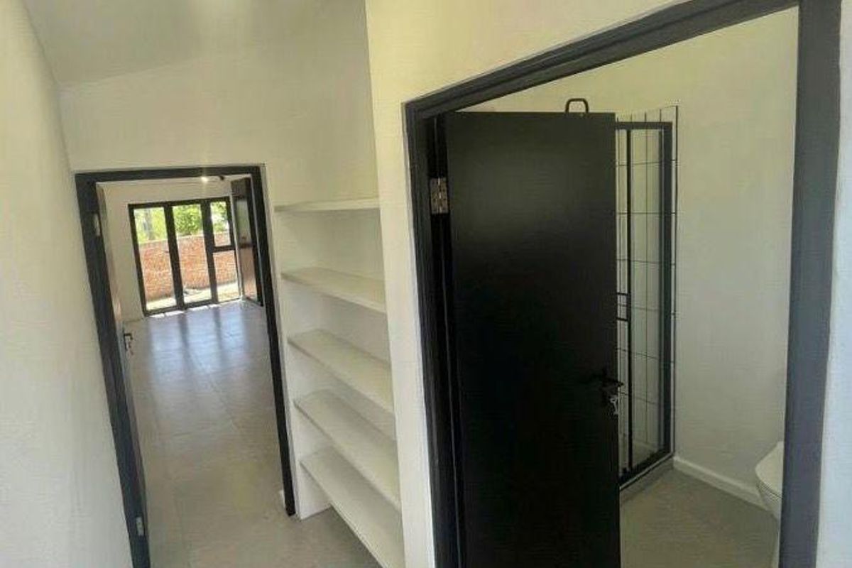 A clean, neutral hallway featuring built-in shelving, tiled flooring, and access to an adjacent bathroom and living area.