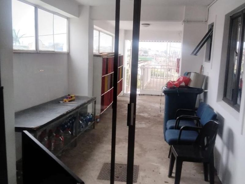 A covered balcony area featuring concrete flooring, sliding glass doors, and metal railings, currently used as a utility and storage space.