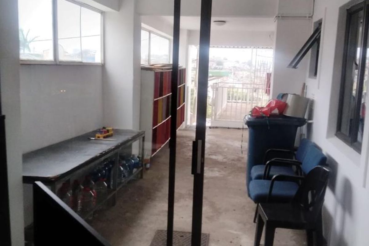 A covered balcony area featuring concrete flooring, sliding glass doors, and metal railings, currently used as a utility and storage space.