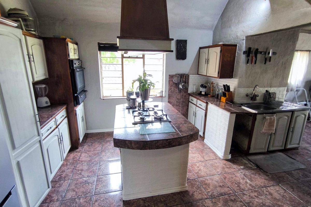 A rustic-style kitchen featuring a central island with a built-in gas hob, tiled countertops, and wooden cabinetry under a vaulted ceiling.