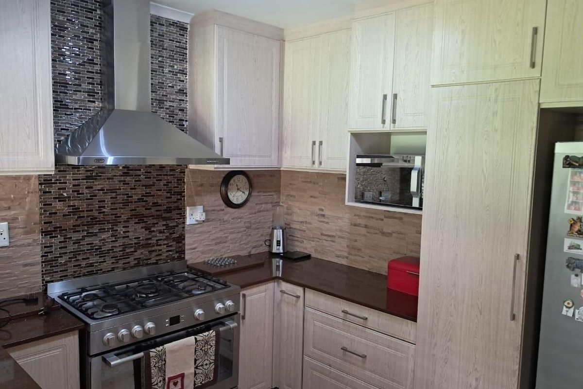 A well-maintained kitchen featuring light wood-grain cabinetry, stone countertops, a gas stove with stainless steel extractor fan, and a decorative mosaic tile backsplash.