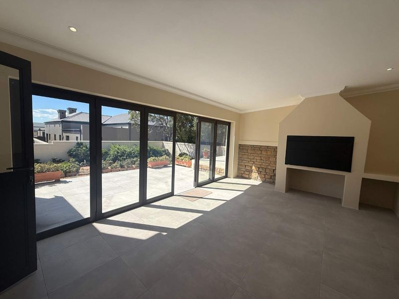 Spacious living area featuring large stacking glass doors opening to a patio, built-in fireplace with stone detailing, and modern tiled flooring.