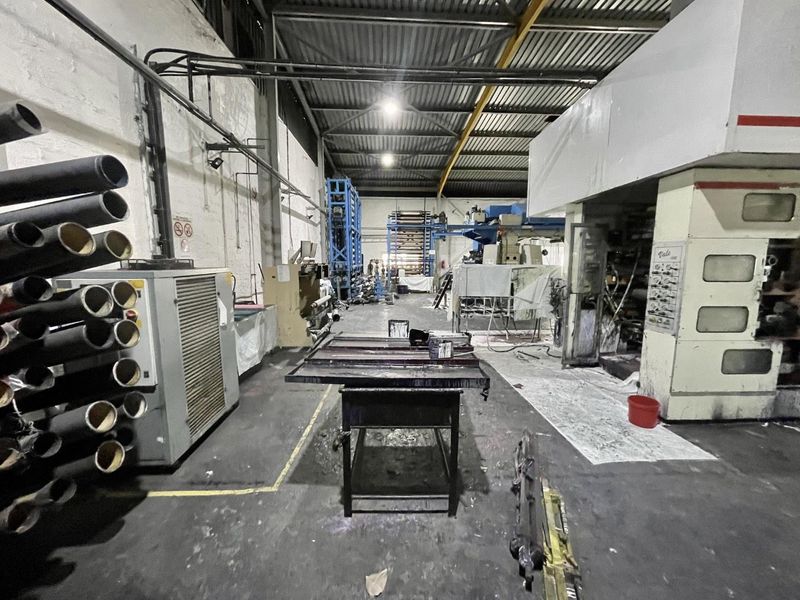 Industrial warehouse space featuring high ceilings with exposed steel trusses, concrete flooring, and integrated heavy-duty manufacturing machinery.