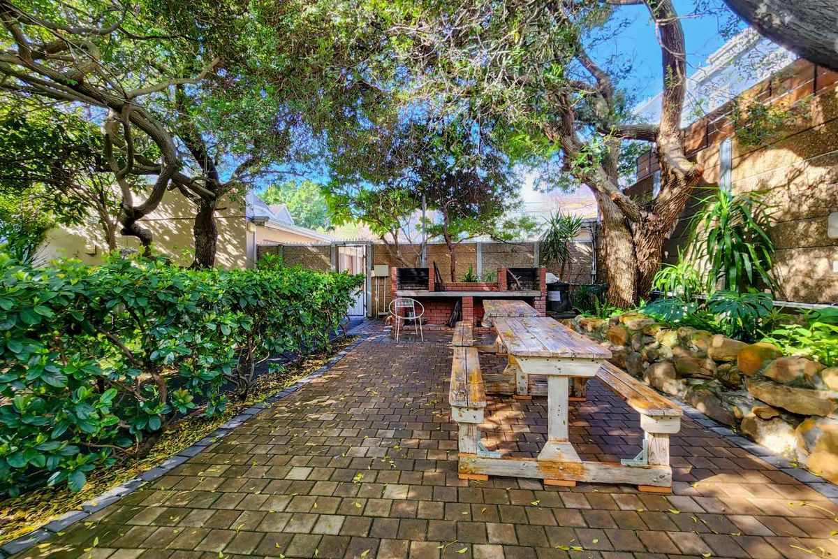 A private rear garden area featuring a brick-paved patio, established trees, and a built-in brick braai, perfect for outdoor entertaining.