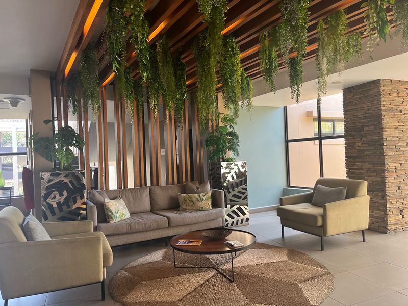 A modern living area featuring a striking timber slat ceiling with integrated lighting, a stone feature wall, and large windows providing natural light.