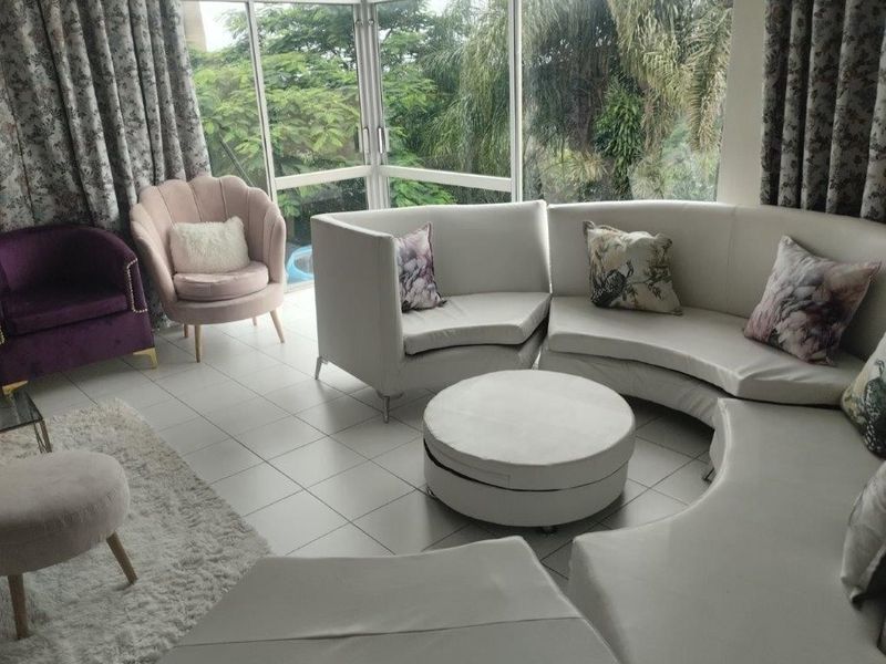 A bright living room featuring large glass windows that provide ample natural light and views of the surrounding greenery.