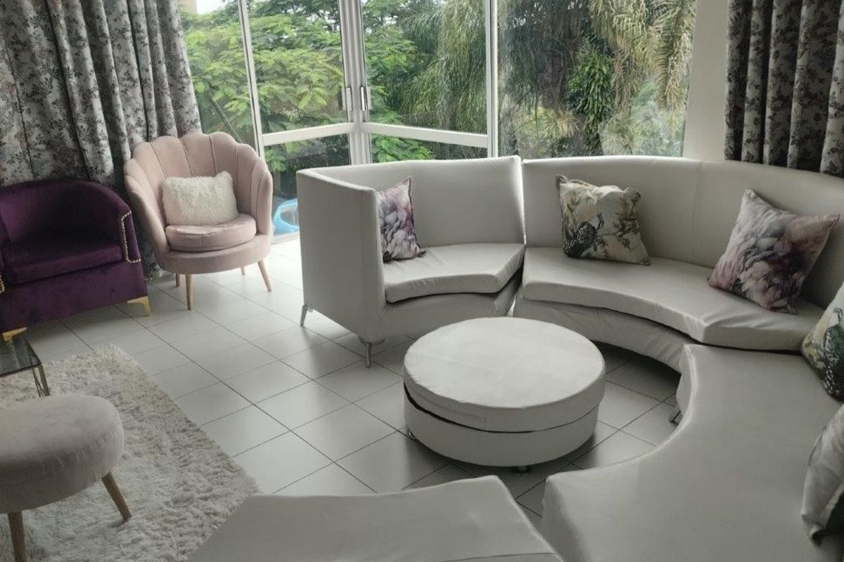 A bright living room featuring large glass windows that provide ample natural light and views of the surrounding greenery.