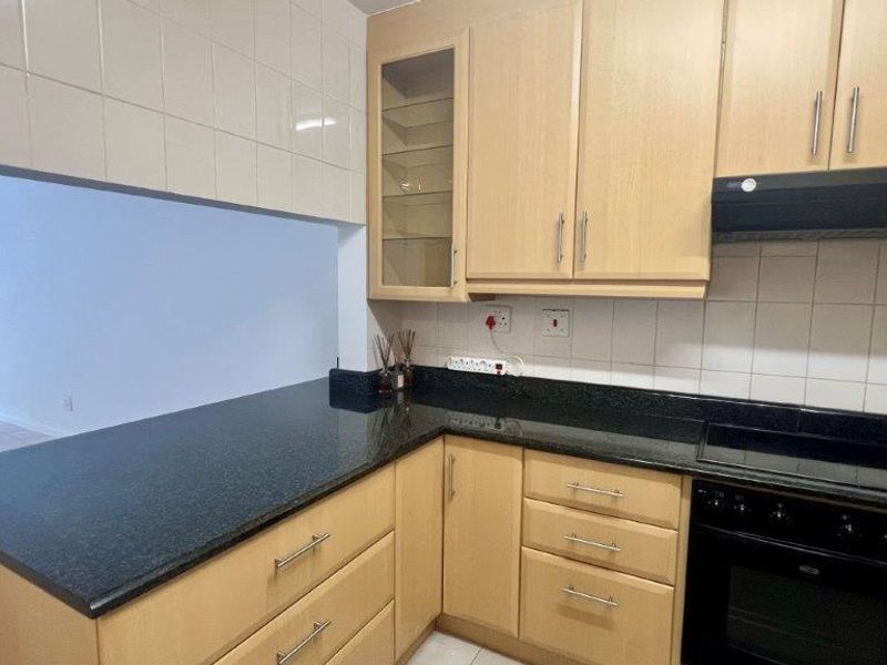 A functional kitchen featuring wooden cabinetry, granite countertops, a built-in oven, and an electric hob with an extractor fan.