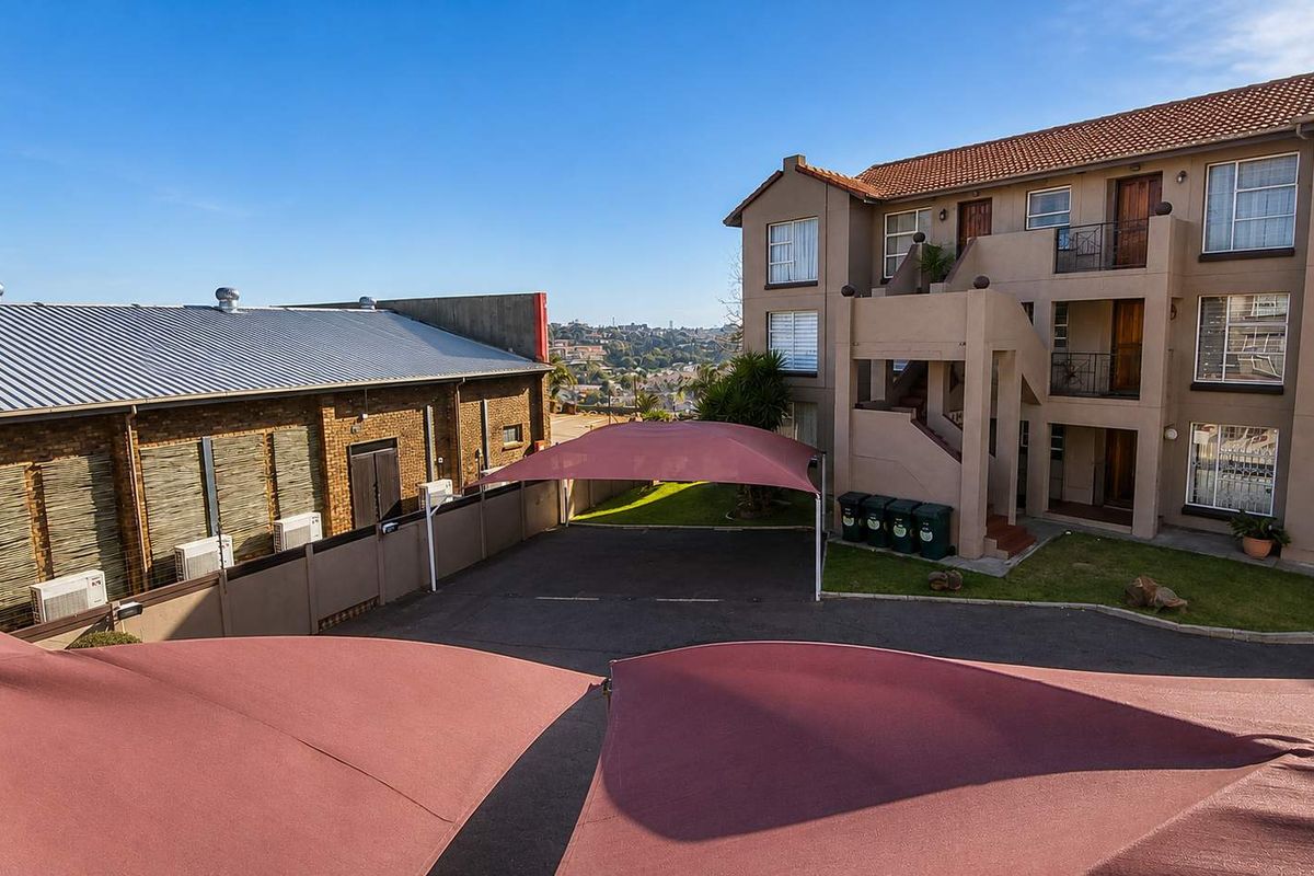 Exterior view of a multi-story townhouse complex featuring a paved parking area with shade sails and landscaped garden space.