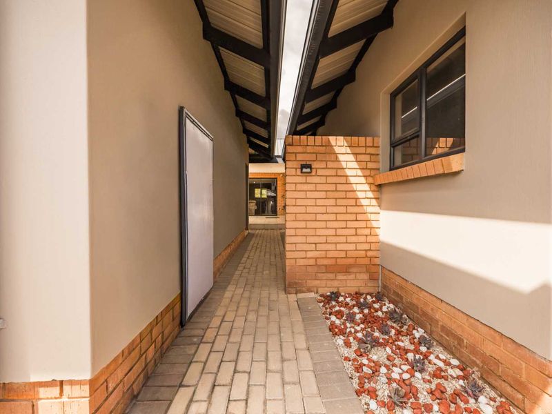 A well-maintained exterior side passage featuring a paved walkway, brick accent wall, and exposed roof rafters, leading towards the rear of the townhouse.