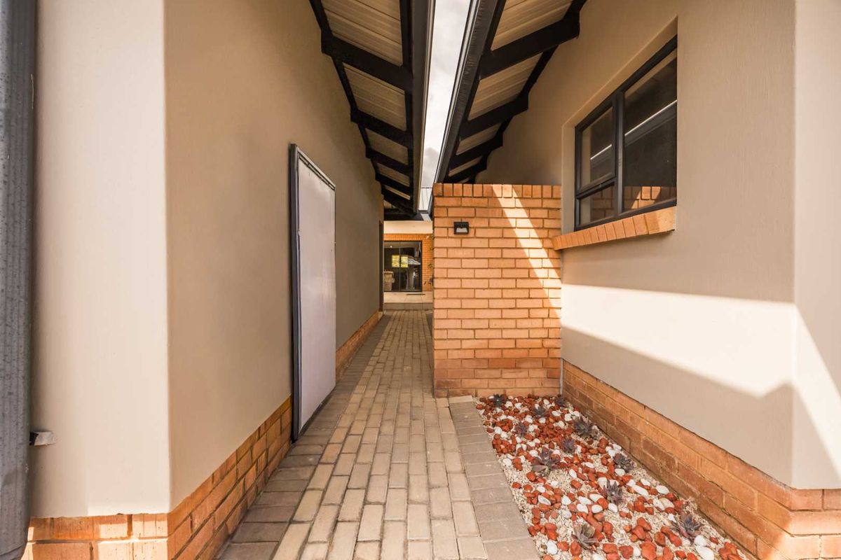 A well-maintained exterior side passage featuring a paved walkway, brick accent wall, and exposed roof rafters, leading towards the rear of the townhouse.