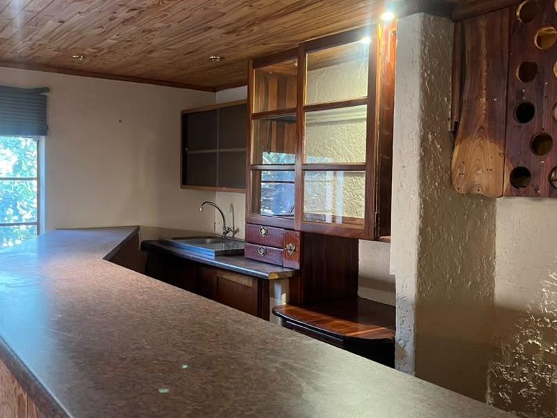 A dedicated bar area featuring a built-in counter, timber ceiling, integrated cabinetry, and a sink, offering potential for a stylish entertainment space.