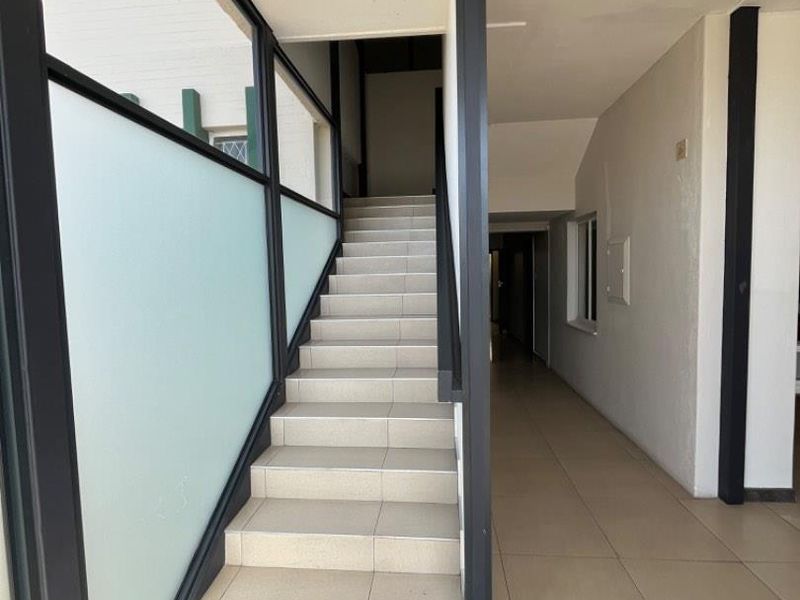 A bright, modern staircase featuring tiled steps, black metal framing, and frosted glass panels, leading to an upper level in a commercial building.