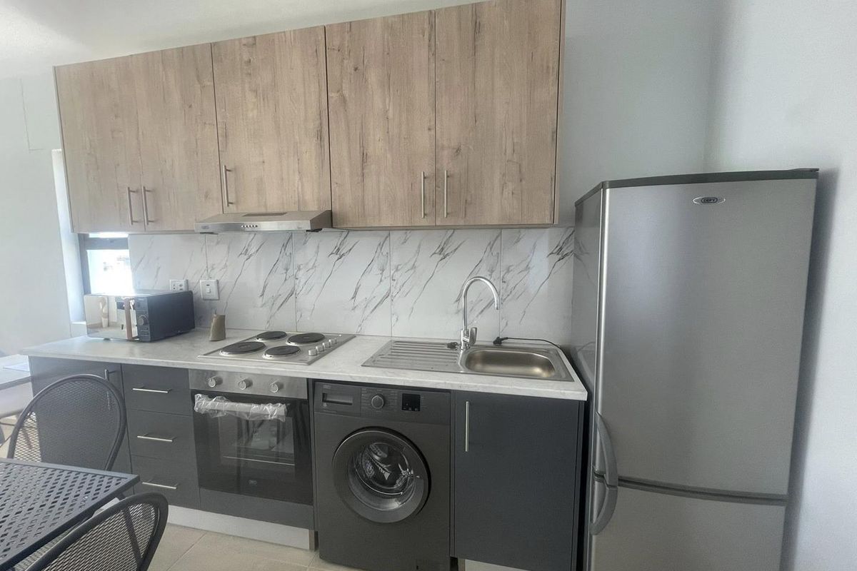 Modern kitchen featuring wood-look upper cabinetry, marble-effect backsplash, integrated oven, hob, extractor fan, and a built-in washing machine.