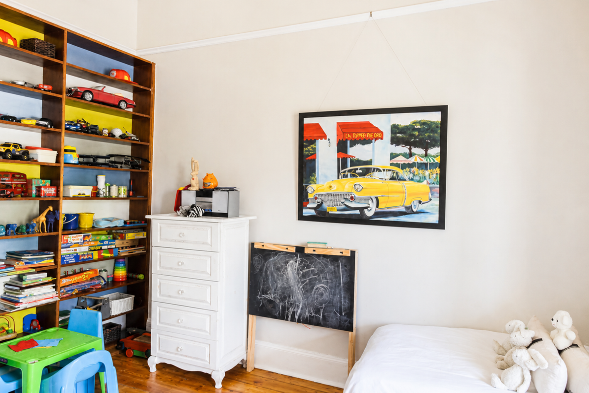 A bright bedroom featuring polished timber flooring, a built-in wooden shelving unit, and classic picture rail detailing.