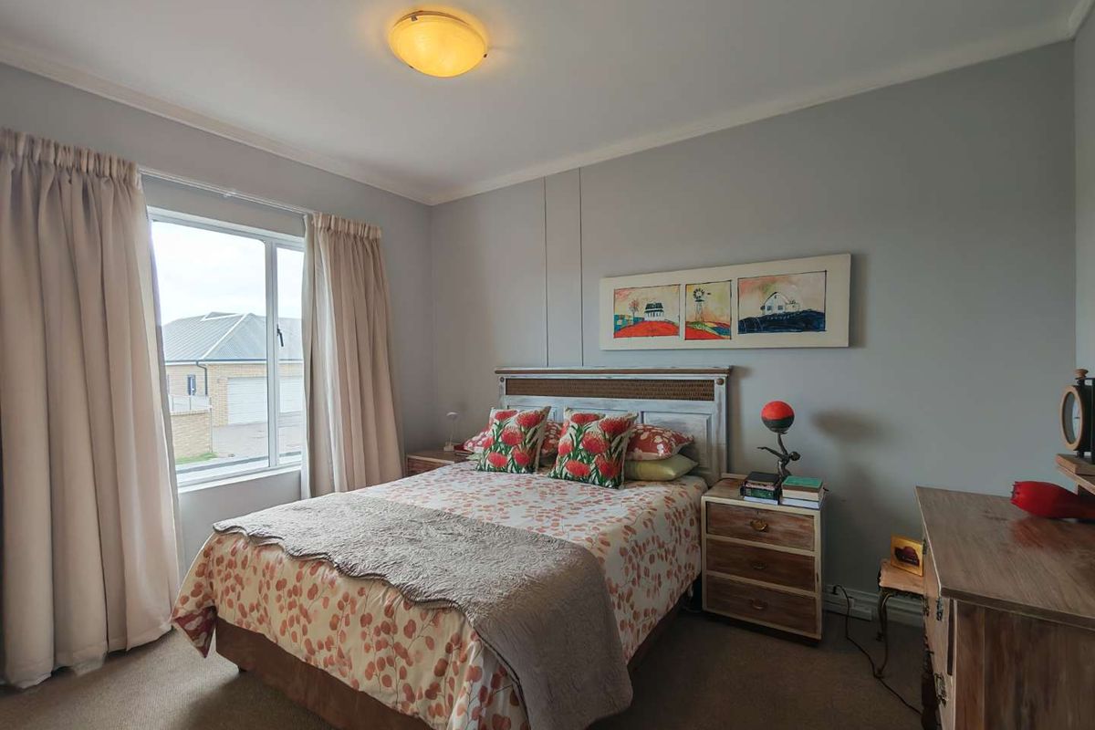 A well-maintained bedroom featuring neutral wall tones, carpeted flooring, and a large window providing natural light.