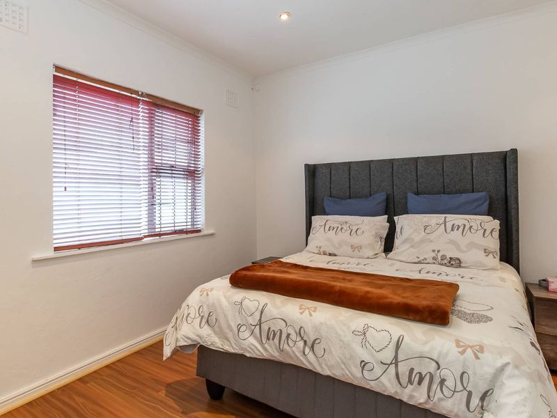 A well-maintained bedroom featuring laminate flooring, recessed downlighting, and venetian blinds, offering a clean and neutral living space.