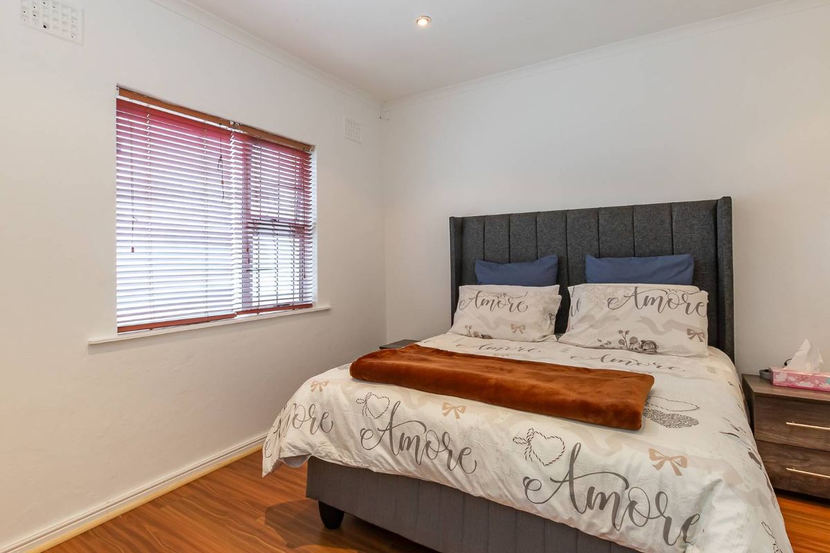 A well-maintained bedroom featuring laminate flooring, recessed downlighting, and venetian blinds, offering a clean and neutral living space.