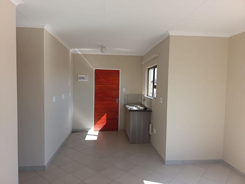 A compact, empty kitchen area featuring tiled flooring, a small kitchenette cabinet with a stainless steel sink, and a timber entrance door.