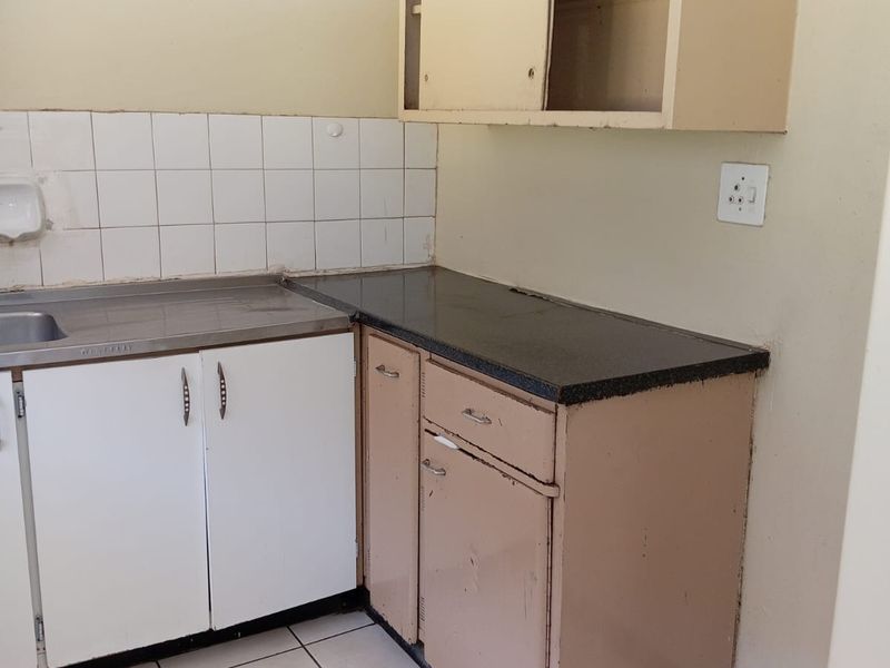 A dated kitchen area featuring original cabinetry, a stainless steel sink, tiled backsplash, and ceramic flooring, offering significant potential for modernization and renovation.