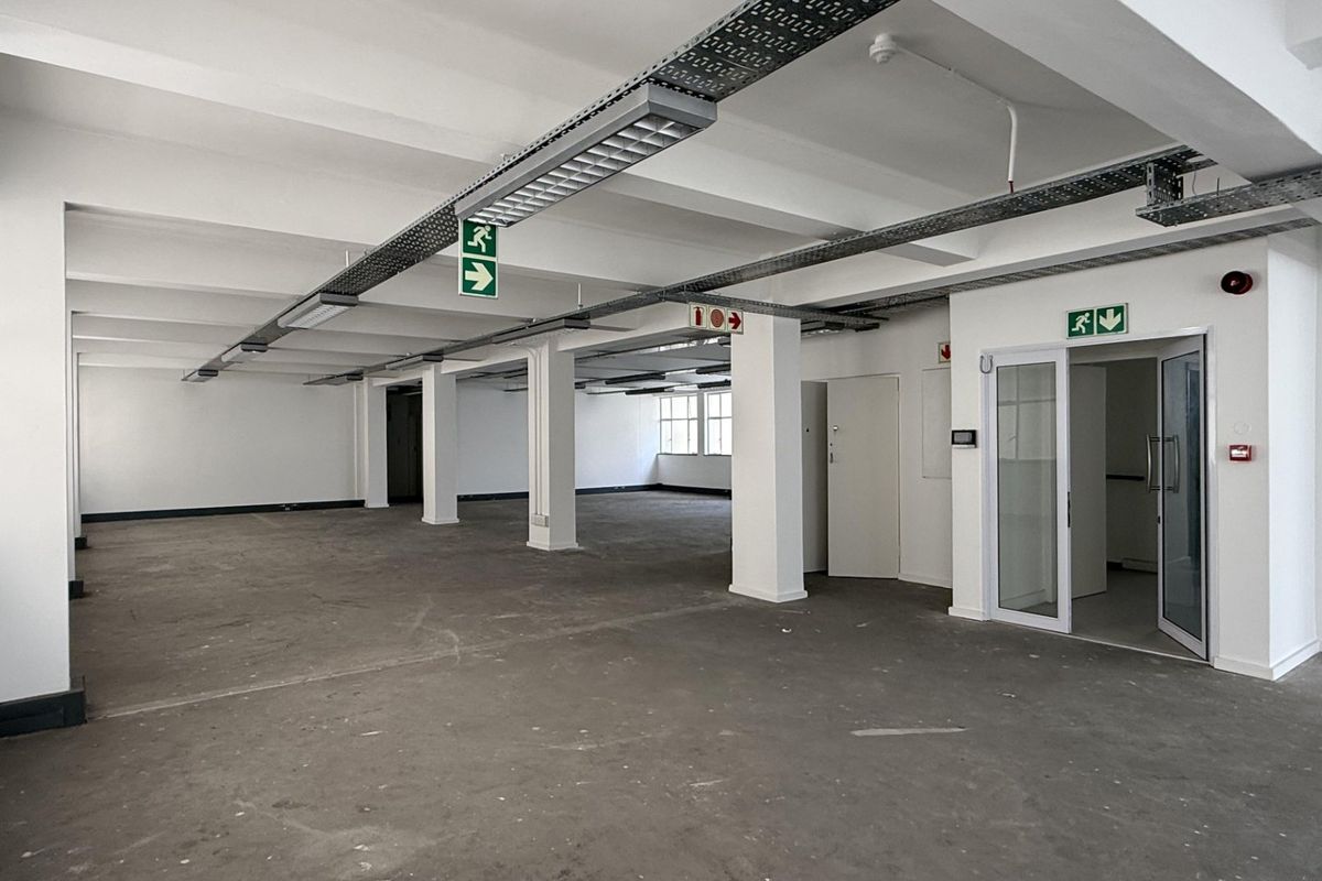 Spacious open-plan office area featuring exposed industrial ceilings, concrete flooring, and integrated emergency safety systems, offering a versatile blank canvas for business operations.
